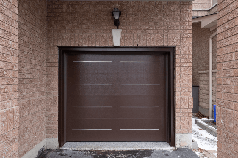 After garage door replacement: modern dark brown garage door with color-matched aluminum capping, exterior view.